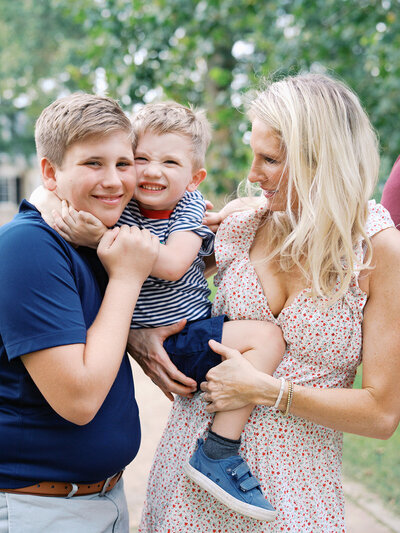 A woman holding and looking at a toddler as the toddler hugs his brother at a Richmond mini session by Katie Stansfield Photography.