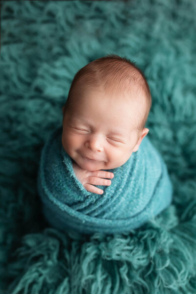 Baby boy wrapped in blue showing a smile.