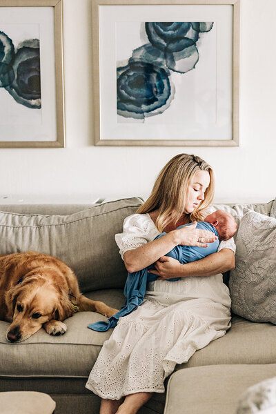 mother holding her newborn baby on the couch with her dog in a well lit livingroom near st pete fl