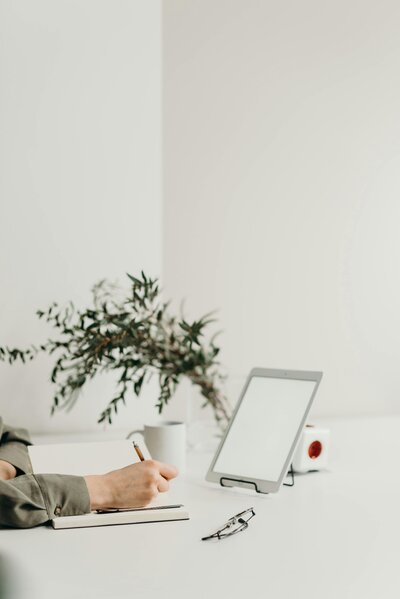 Woman writing in a notebook with Ipad in the background