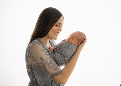 woman wearing a blue lace dress holding her baby and smiling down at him