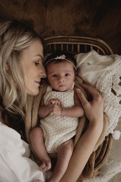 A woman cuddling with a baby wrapped in a soft blanket, both lying on a wicker chair.