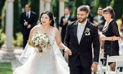 Bride and groom smiling while walking after outdoor ceremony with flowers | Summer Wedding at The Hamilton Manor | Hamilton Township, New Jersey