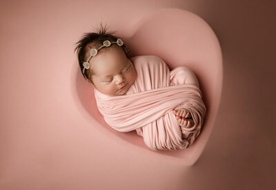 Newborn baby girl swaddled in blush pink wrap on rounds cushion - luxury newborn photography in Maple Grove Minnesota