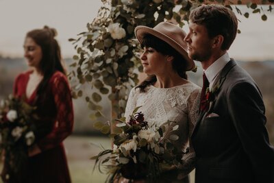 Bride with long veil and groom in gray suit holding hands & looking in opposite directions featured by Black Bride at Cornman Farms