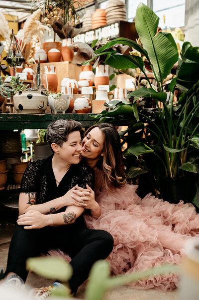 Couples Photography, LGBTQIA+ couple wrapped in each other 's arms surrounded by pottery and greenery.