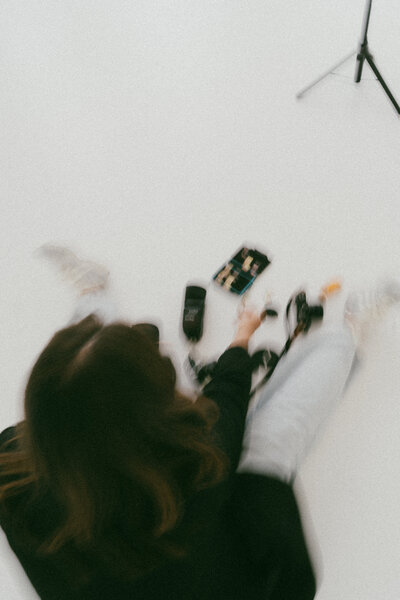Blurry overhead image of a female photographer sitting on the floor surrounded by film cameras, light meters, and photography gear.