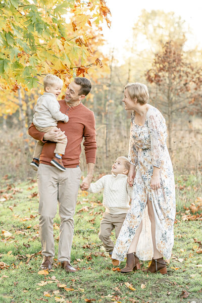 Family of four holding hands and all looking at the youngest boy and laughing during fall family portrait session.