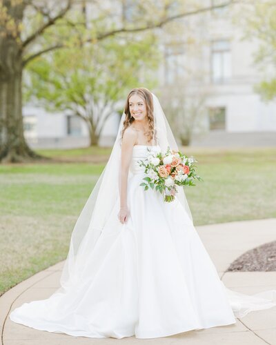 A bride smiles over her shoulder while walking on a sidewalk with a colorful bouquet captured by an Little Rock wedding photographer