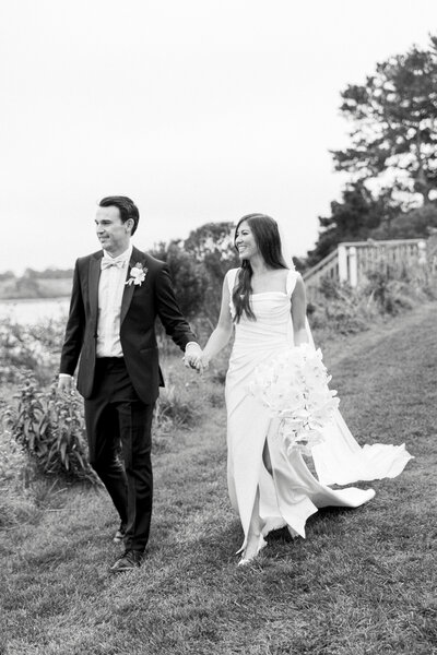 Elopement Photographer, hand in hand, a bride and groom walk down a grassy embankment near the beach