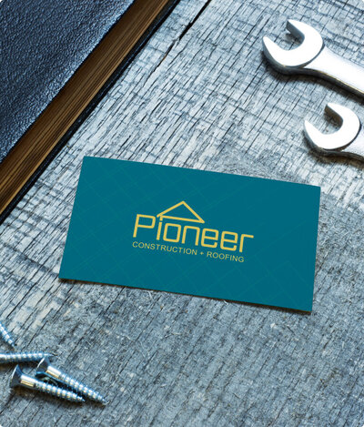 Front facing business card of Pioneer Construction laying on table surrounded by nails and wrenches.