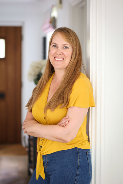 Photo of Stacey, blonde hair, bright yellow top, leaning against a door frame