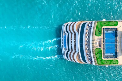 Overhead shot of an ocean cruiseliner sailing through bright blue waters.