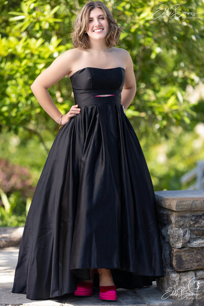 A young woman poses outdoors in a black gown with bright pink shoes, photographed by a Simpsonville photographer."