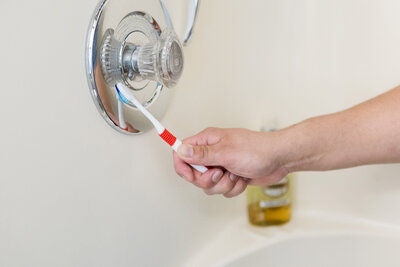 Professional cleaner cleaning faucet in bathroom