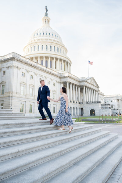 The couple in the image are holding hands walking up the steps of the DC capitol building. They are looking at each other as they walk. 