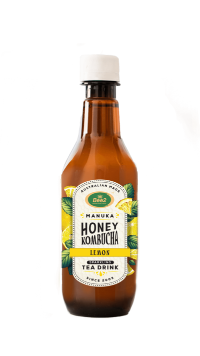 A brown glass bottle of Manuka Honey Kombucha, featuring a label with green and gold accents and the words "Raw Fermented Tea Drink." The label highlights the use of Manuka honey, with vibrant illustrations of honeycombs and leaves, emphasizing the natural and organic ingredients.