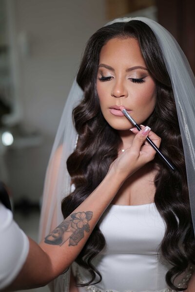 Luxury bridal makeup artist in NYC applying makeup to a beautiful bride in a white wedding dress using a favorite brush.