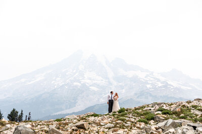 A bride and groom are standing in front of a mountain in the distance