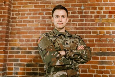 man in army apparel standing in front of a brick wall