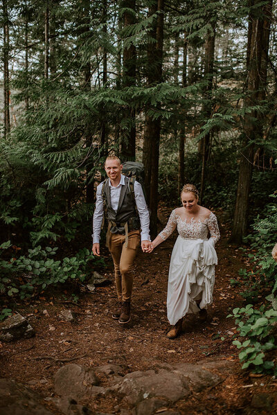 Couple walking hand in hand on a forest trail during their hike on their elopement day.