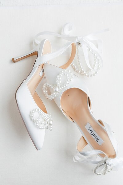 Brides white shoes with gold and white pearls sit on a stool.