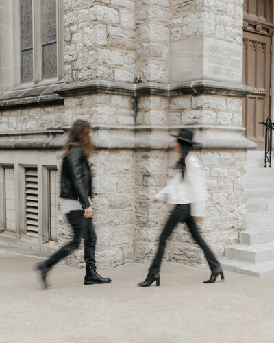 blurred photo of couple in leather jackets walking by eachother in front of old brick building