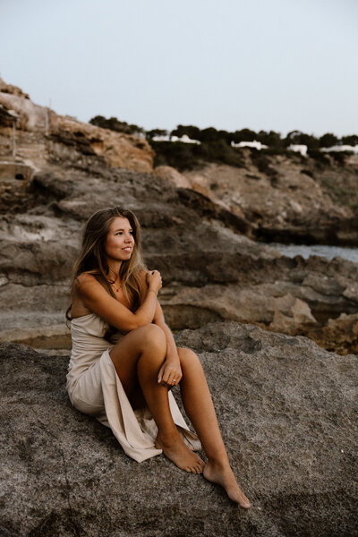 Photographer is sitting on the rocks on Ibiza posing for personal branding photography on Ibiza