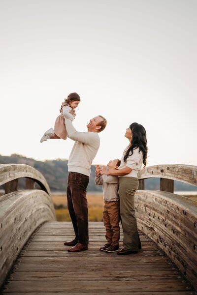 dad lifts toddler while mom and son watch. they are on the iconic martinez arch bridge near walnut creek ca