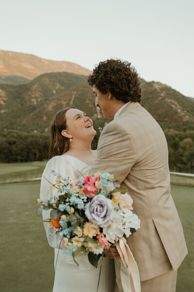 A photo of a bride and groom taken by Bailee Freeman Photography on a golf course. Green mountains behind the bridal couple. 