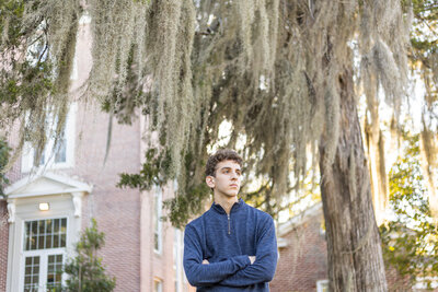 Senior boy with arms crossed under big tree with moss