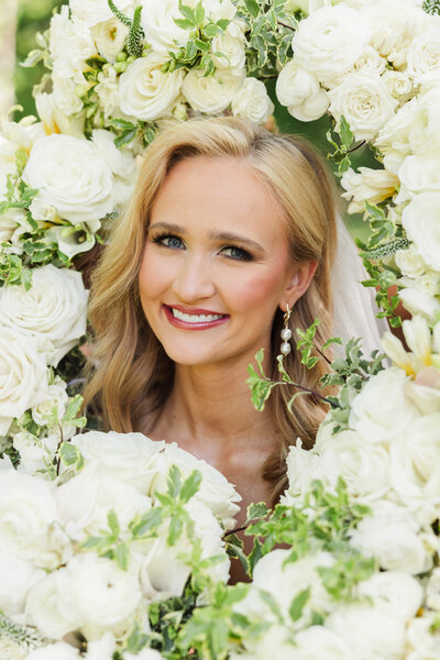 A smiling newlywd bride is surrounded by bouquets of white roses