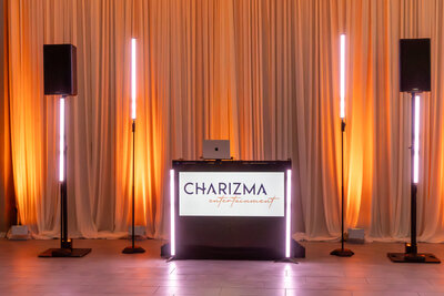Sleek DJ booth with up-lighting and branded Charizma sign, set against curtain backdrop.