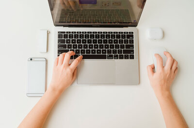A Google Ads expert working on a one-time ads setup service using a laptop on a white desk, with a cellphone as an additional tool.