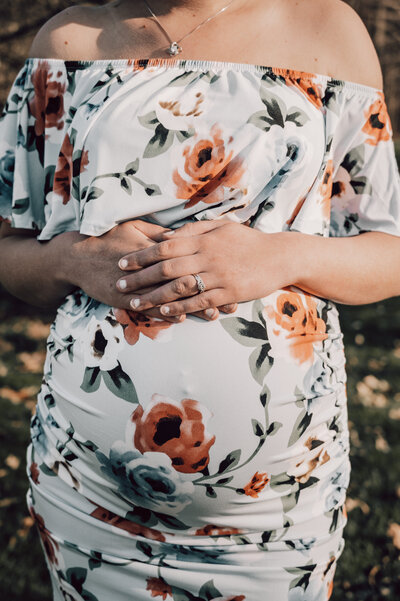 Mom with hands on pregnant belly in a floral dress