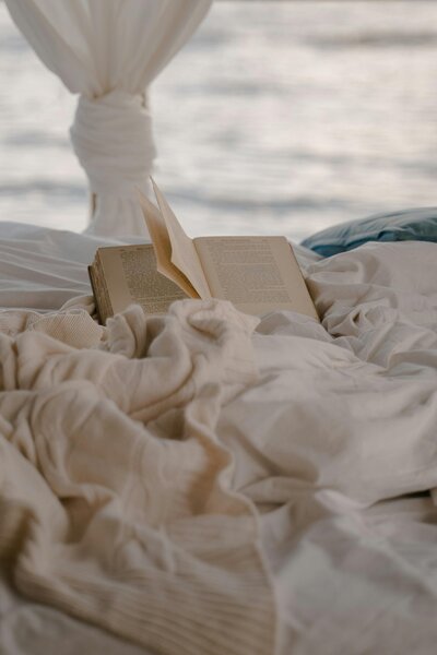 A book laying on crumpled sheets with a sea view