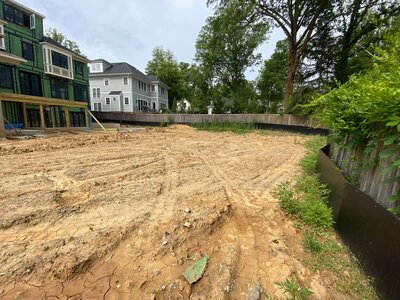 Backyard under construction with exposed dirt, uneven terrain, and a partially installed retaining wall, surrounded by neighboring houses.