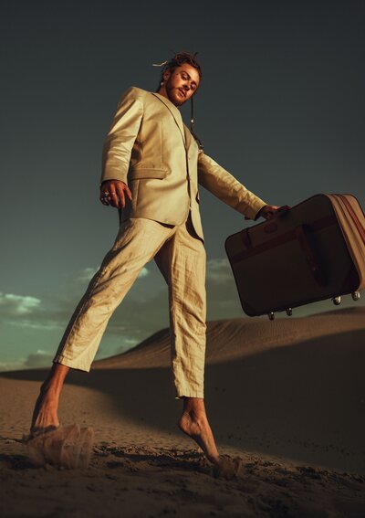 man posing with brief case, barefoot in sand, cream suit, brief case