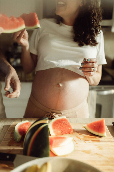 A pregnant mother eating a water melon and giggling.