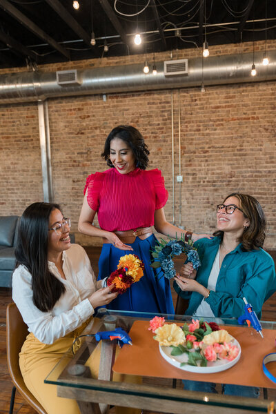 The transformative journey as three women embrace their Glow-Up in our craft workshop. Seated with wreaths of flowers in their hands, each creation reflects personal growth and artistic expression.