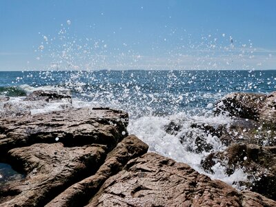 Ocean waves splashing against rocks with a blue sky in the background