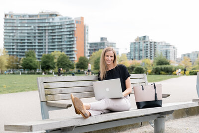Blonde women in black shirt and beige pants using laptop on a bench