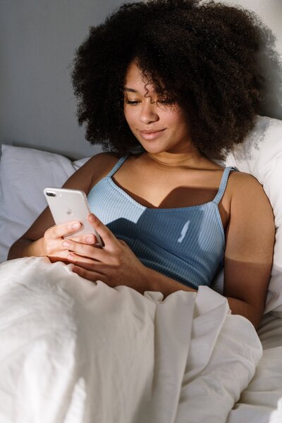 Black woman lying in bed looking at phone