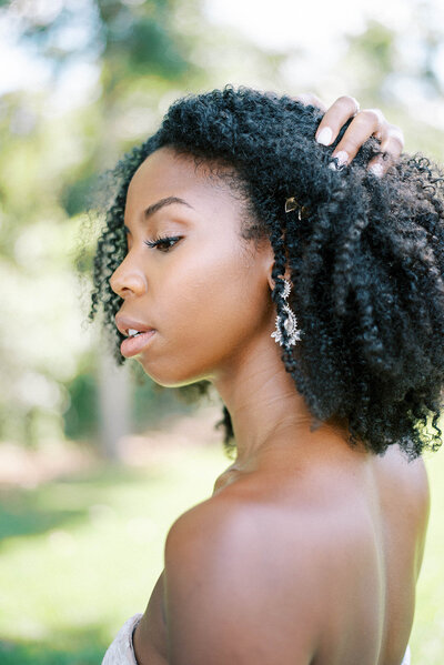 black bride holding her curls back to show she cheek bones and unique wedding earrings.