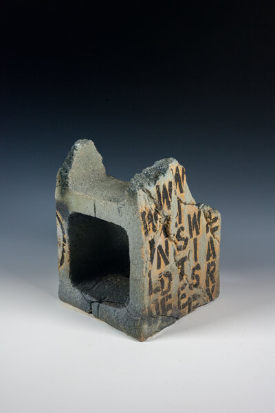 A cinder block that was hand made out of clay is decorated with underglaze to resemble graffiti and various other imagery