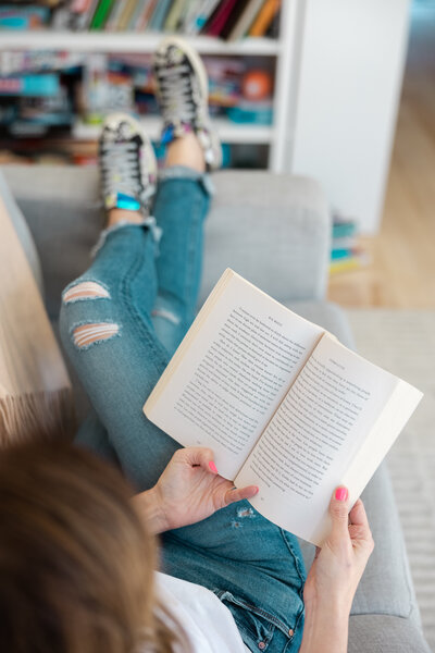 Close up of a woman holding a book open on the couch.