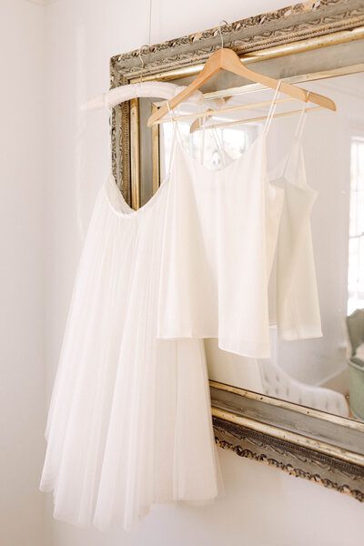 The bride’s silk slip and bridal tank top elegantly hanging on a vintage mirror, captured in soft natural light before an intimate backyard wedding in Richmond, Virginia.