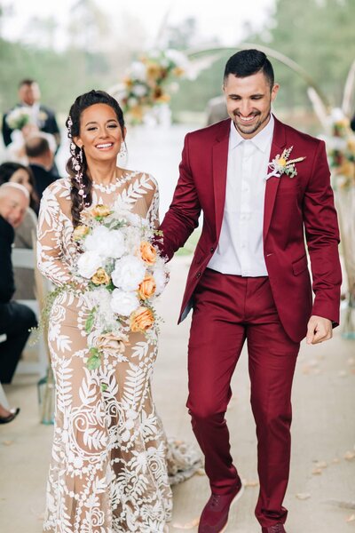 A bride and groom walking down the aisle in a burgundy suit, captured by Britt Elizabeth destination wedding photography.