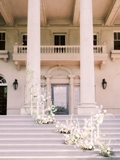 A grand staircase with white floral arrangements leads up to a large building with tall white columns and a central double door—perfect for any vision a Banff wedding planner might bring to life.