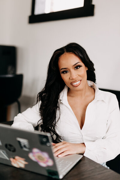 Tiara in a white top typing on her laptop at a table